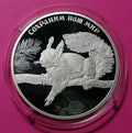 2023 3 Rubles Silver coin Red Squirrel Series: Protect Our World
A round silver coin featuring an engraved squirrel on a branch with pine needles, displayed inside a clear protective capsule against a bright pink background. The coin has Cyrillic text along the top edge.