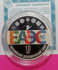 A 10-year Russian Federation Economic Union commemorative coin in a clear plastic protective capsule, displayed on its original blue and white authenticity certificate against a bright pink background.